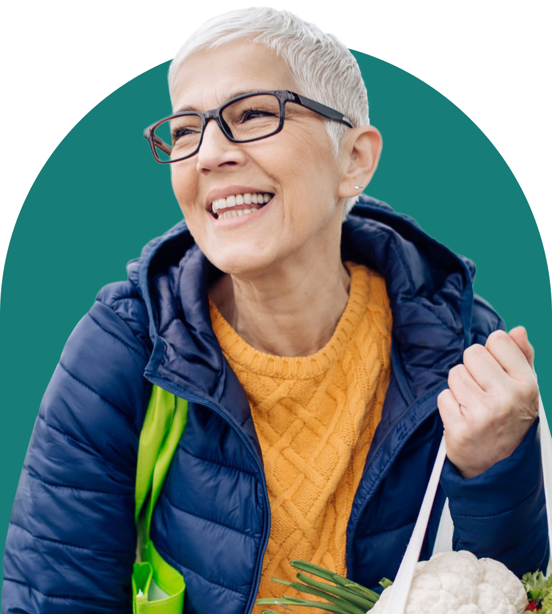 older-woman-smiling-wearing-glasses-holding-grocery-bags-wearing-blue-jacket