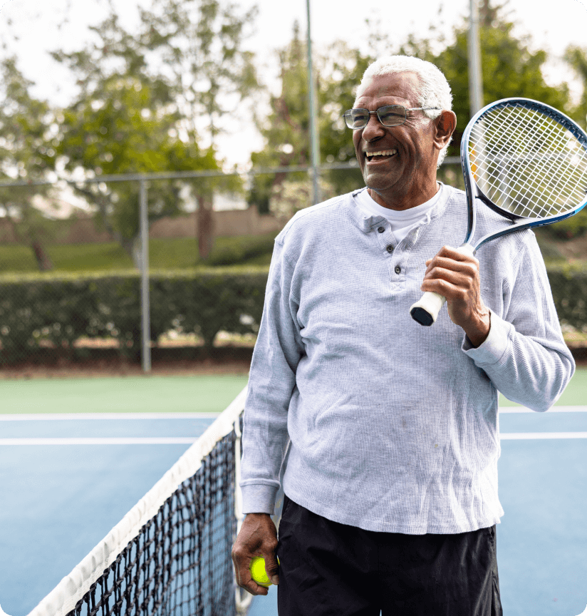 A man with white hair holding a tennis racket and laughing