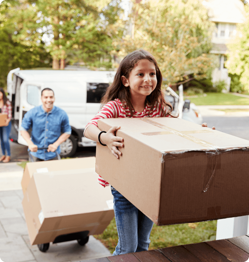 A young girl carrying a moving box into a house