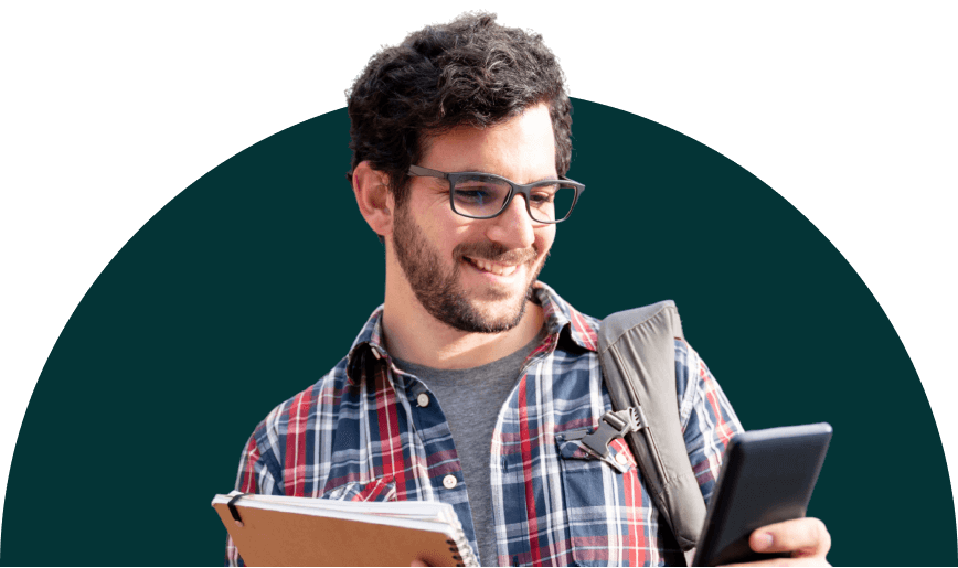 An international student smiling at his mobile device while also carrying a notebook