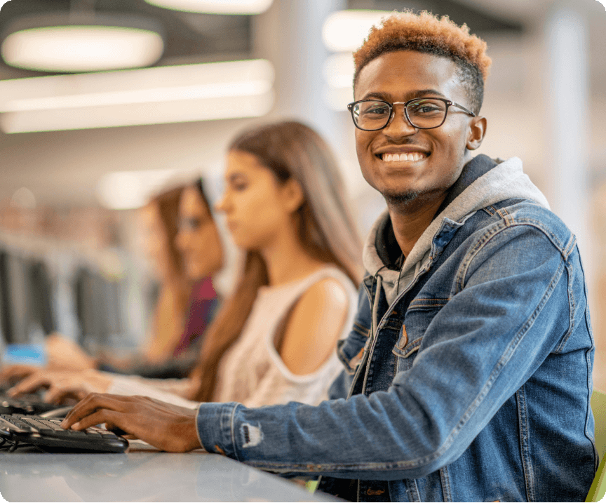 A row of smiling international students typing at a communal desk in a computer lab