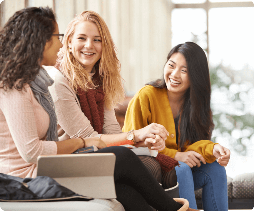 Three female international students sitting on a couch chatting and smiling